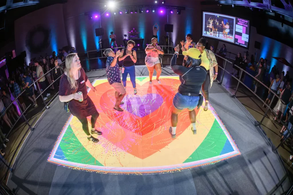 A group dancing on an LED stage with rainbow hearts on it