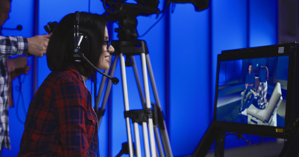 Female event producer is wearing a headset and sitting behind the camera.