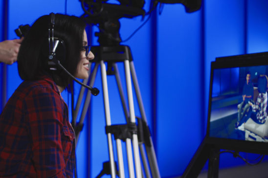 Female event producer is wearing a headset and sitting behind the camera.